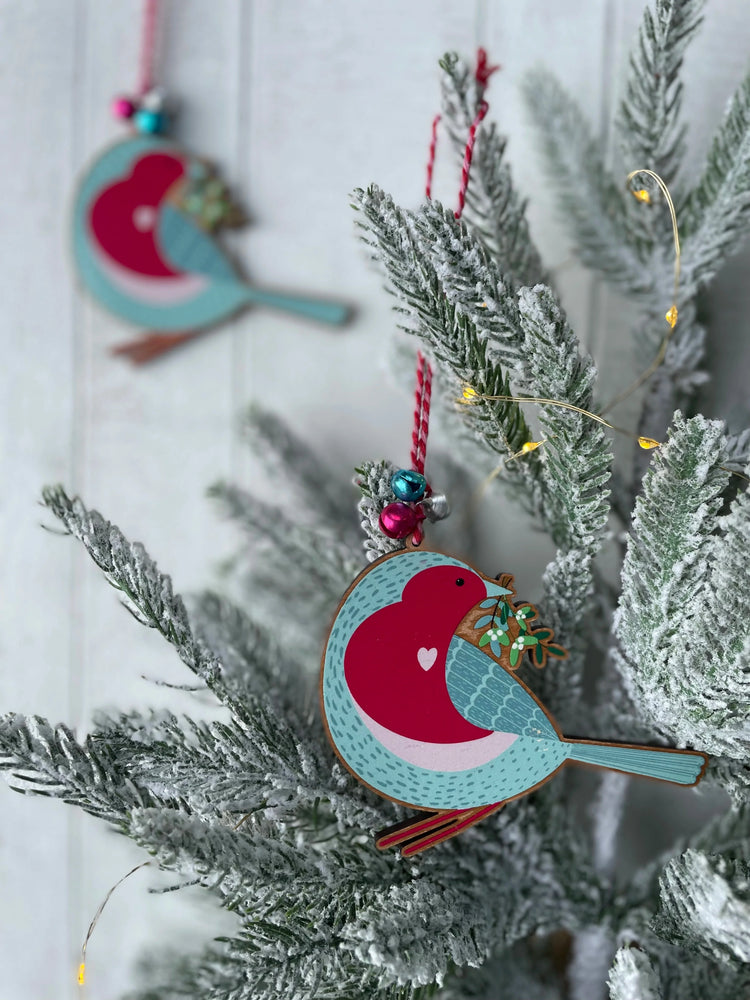 Eco-friendly wooden robin Christmas tree decoration by Sister Sister, with raspberry breast and mistletoe detail, hanging on snowy festive tree with jingle bells